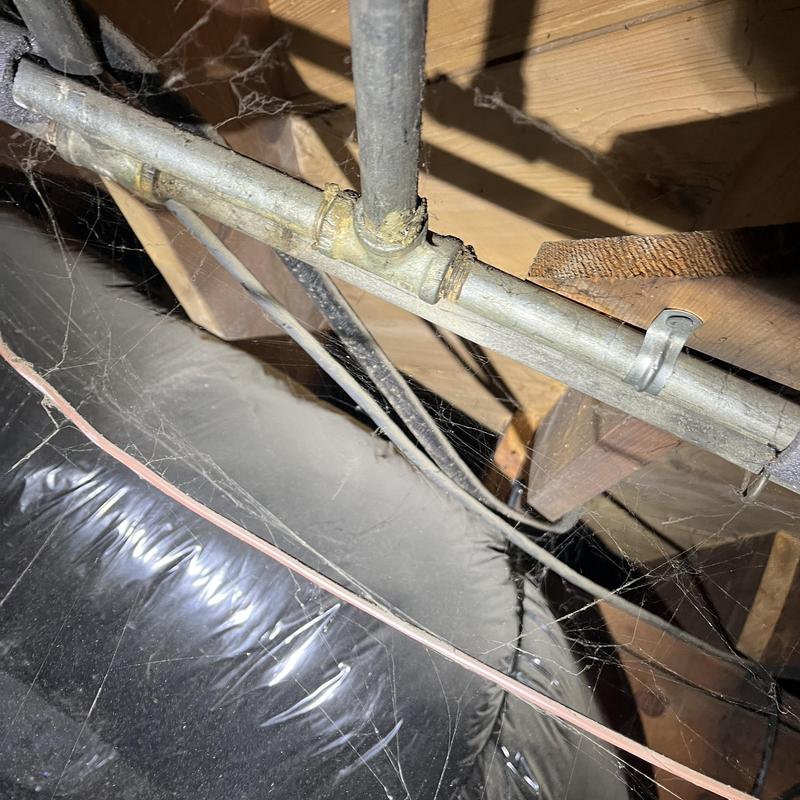 Galvanized plumbing pipes in crawl space with cobwebs