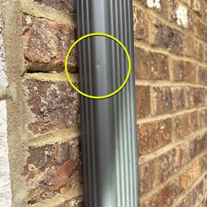 Metal downspout dent with circled damage on brick wall