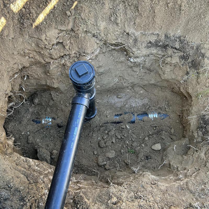 Black plastic drain pipe with cleanout in dug trench