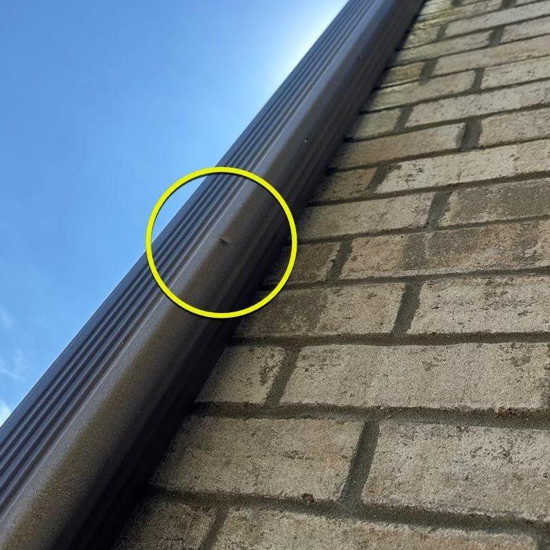 Metal gutter dent with impact damage marked in yellow circle