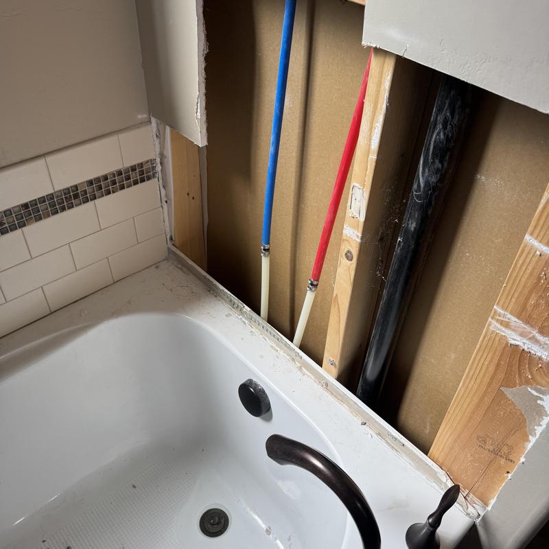 Tub faucet and plumbing pipes behind wall panel removed