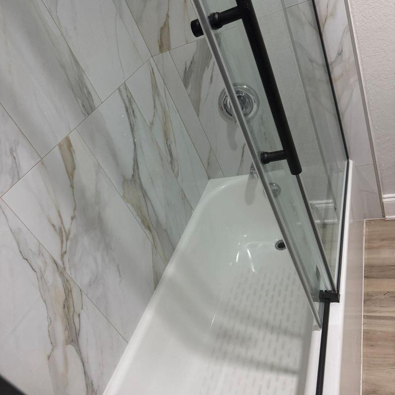 Bathtub with glass shower door and marble tile walls