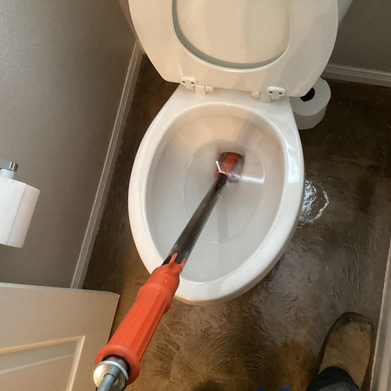 Toilet drain auger clearing blockage in bathroom toilet bowl