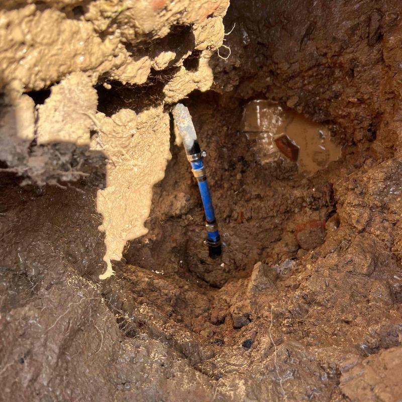 Underground water pipe leak exposed in soil hole