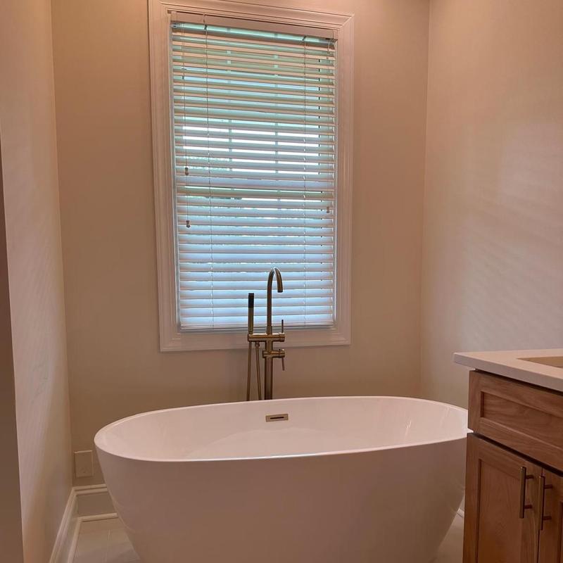 Freestanding bathtub with floor-mounted faucet and window blinds