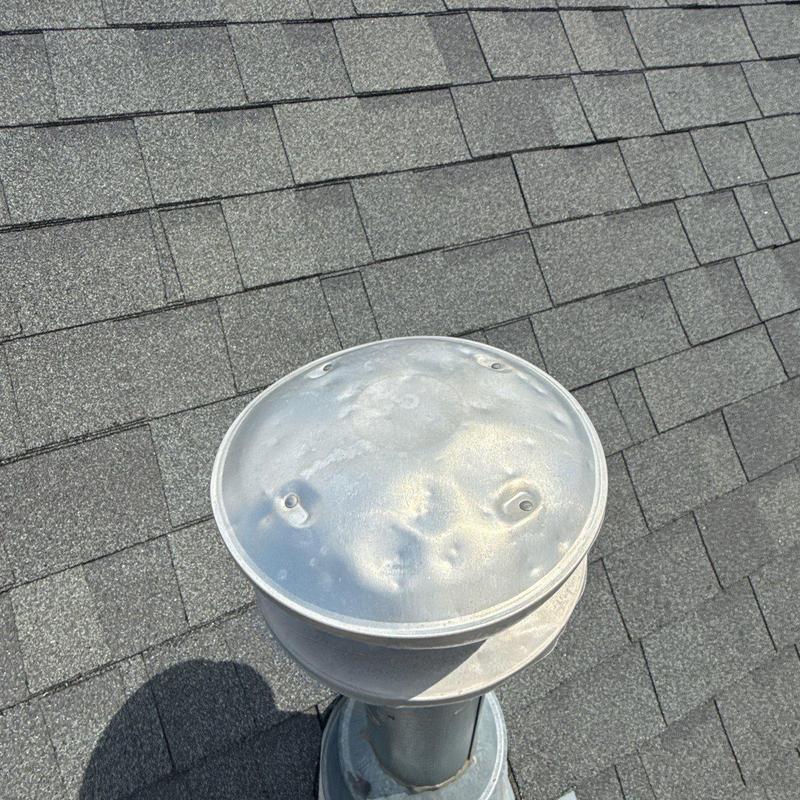 Roof vent cover with hail damage dents on shingle roof