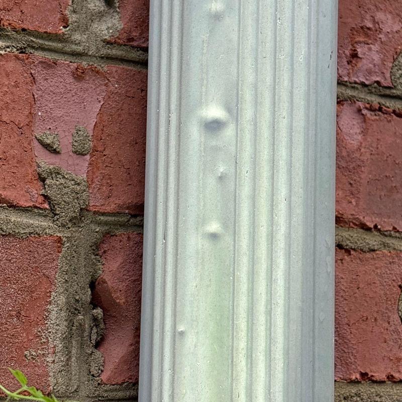 Metal downspout with hail dents on brick wall background