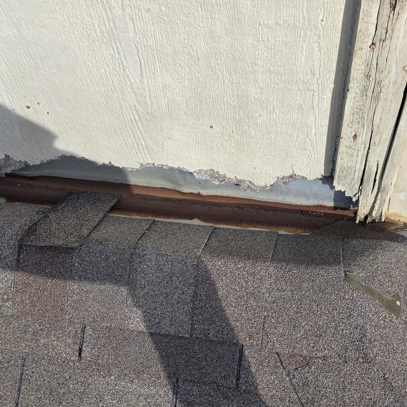 Roof flashing with rust and shingle damage near wall base