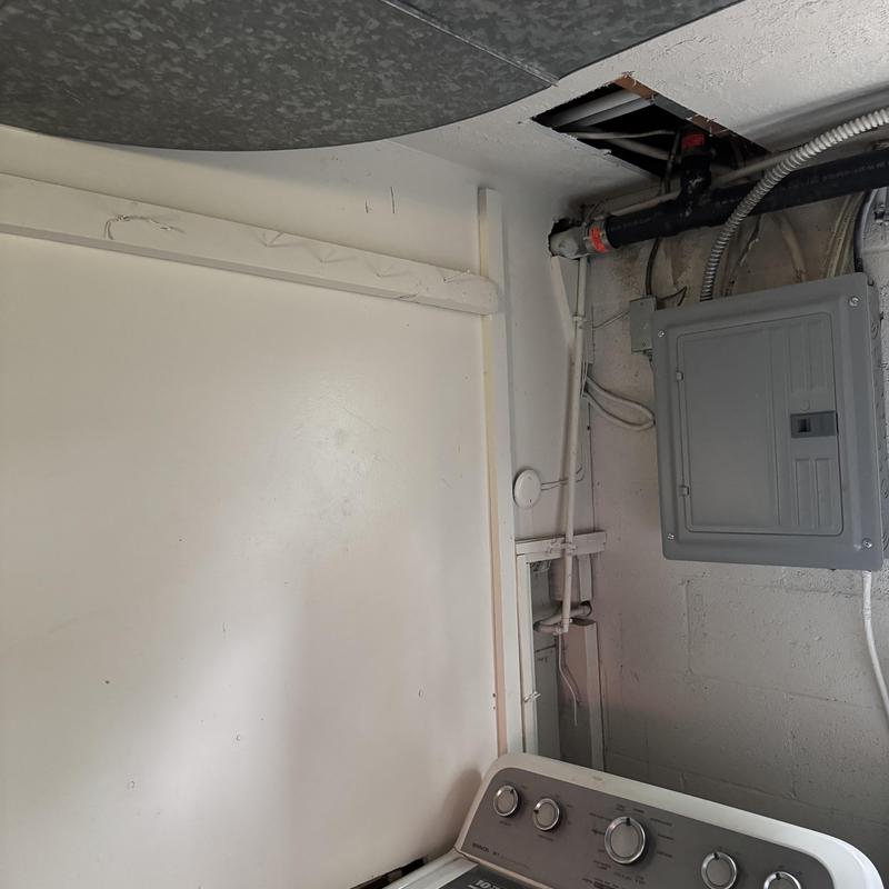 Electrical panel next to laundry area and ceiling pipes