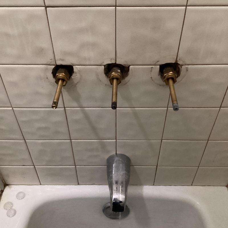Three-handle shower valve stems exposed in tiled wall