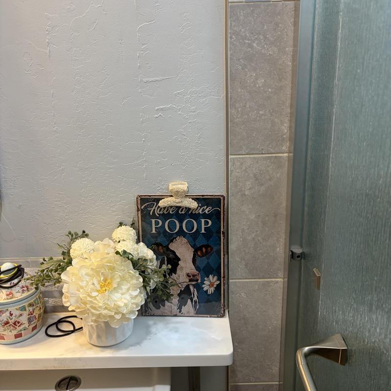 Bathroom decor with flower arrangement and humorous sign