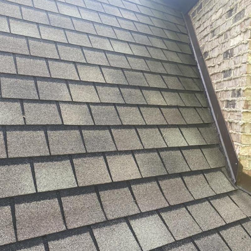 Designer asphalt shingles on sloped roof near brick wall