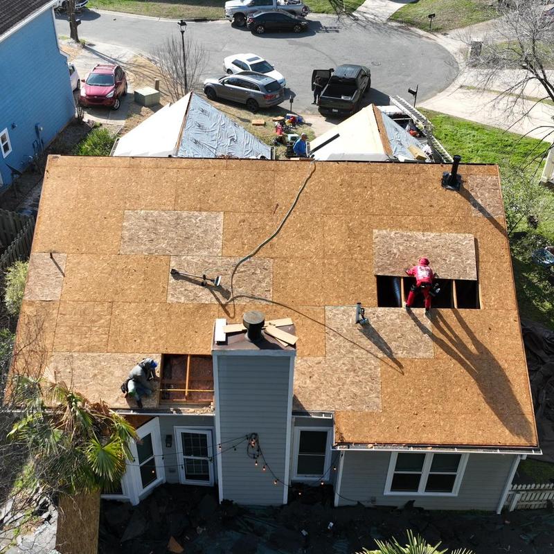 Roof deck plywood installation with chimney and workers