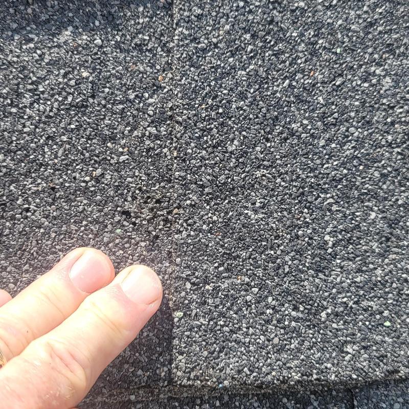 Asphalt roof shingle hail damage close-up with fingers