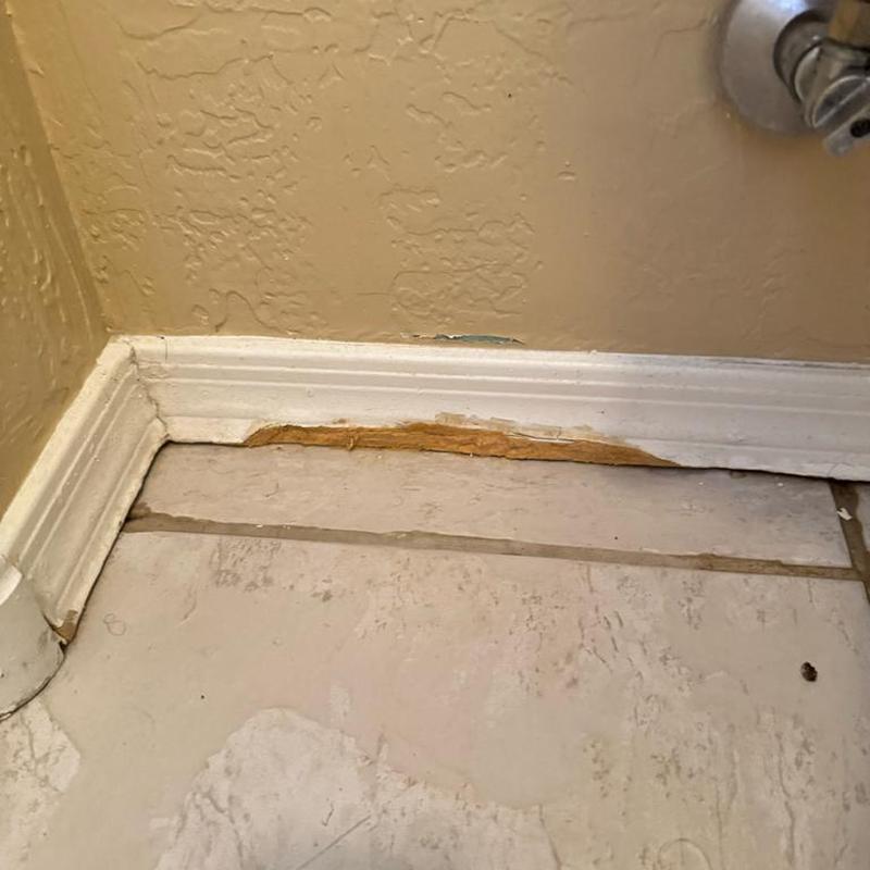 Baseboard with water damage near bathroom tile floor