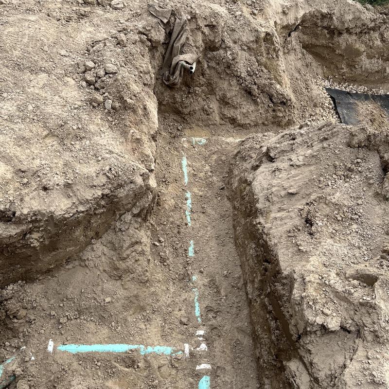 Drain field trench excavation with marked pipe lines