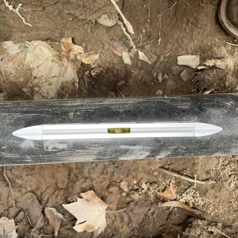 Main sewer line with level tool in dirt trench