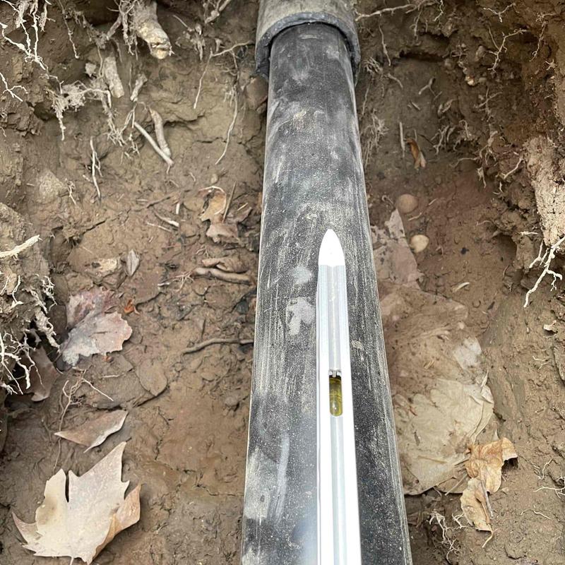 Main sewer line with level tool in dirt trench