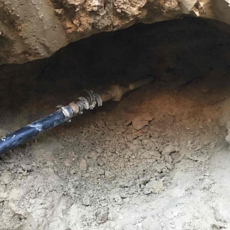 Black poly water service line in dirt hole with clamps