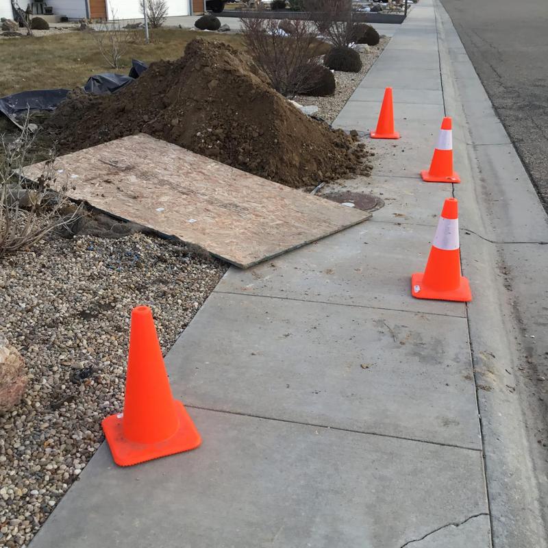 Water meter hole dug with safety cones on sidewalk