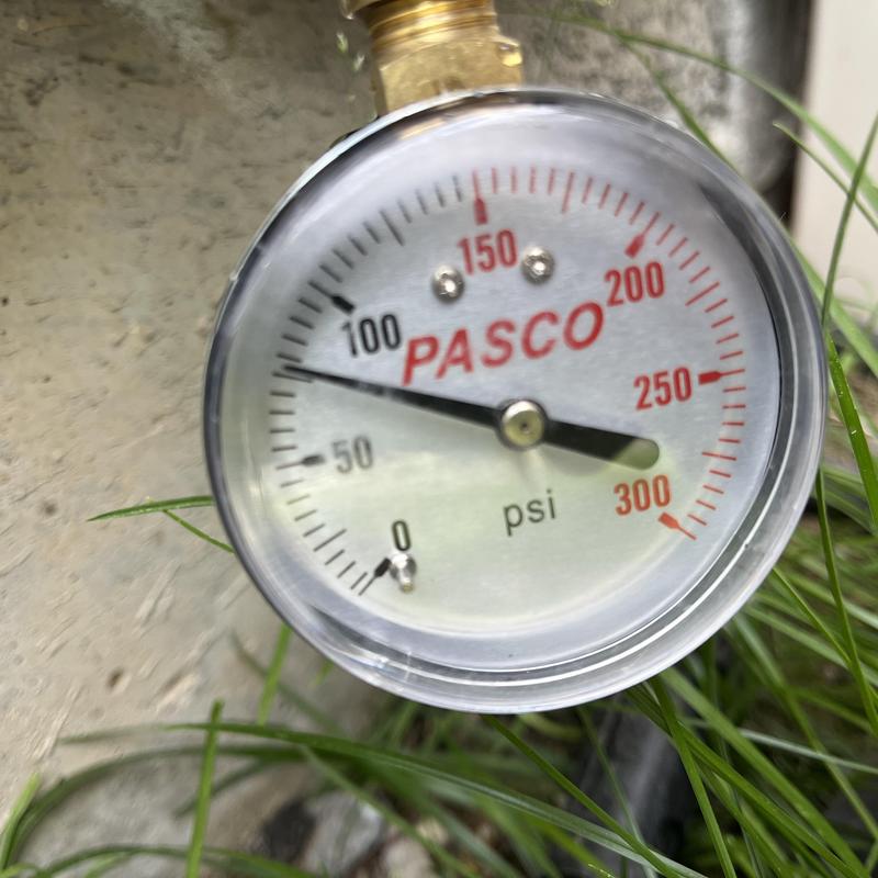 Water pressure gauge showing PSI near grass and concrete