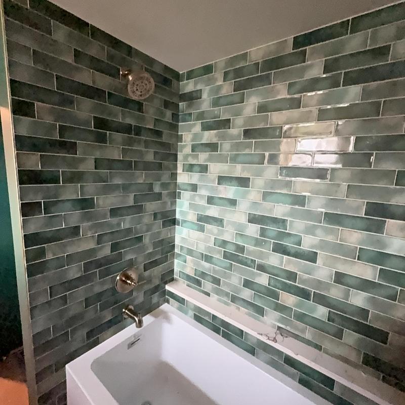 Bathroom tub and shower fixtures with green tile wall