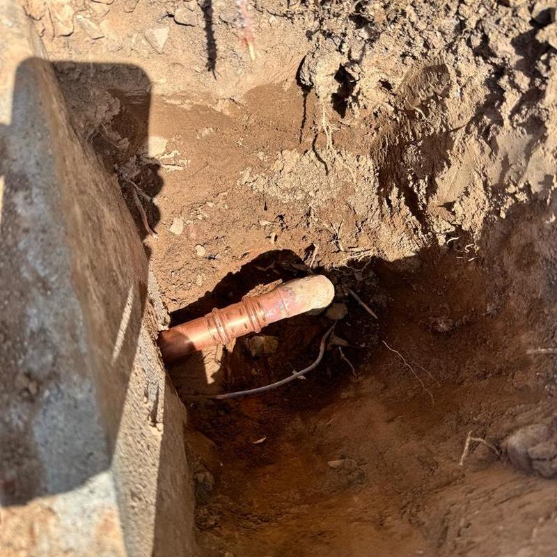 Copper water main pipe exposed in dirt trench repair