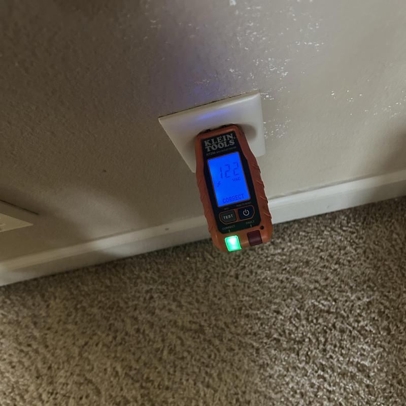 Electrical outlet tester plugged into wall outlet with voltage reading