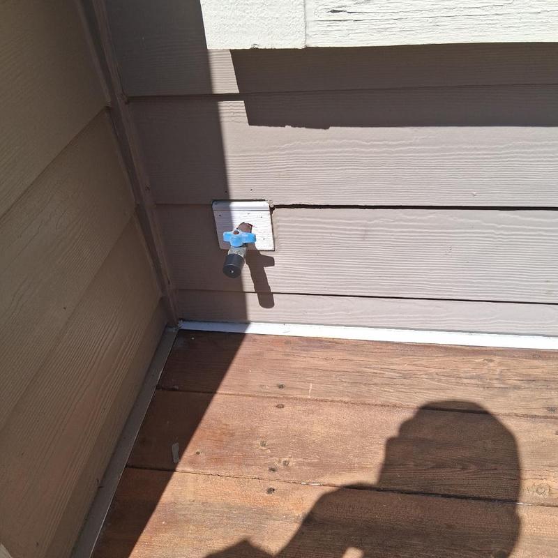 Outdoor water spigot with blue handle on siding wall