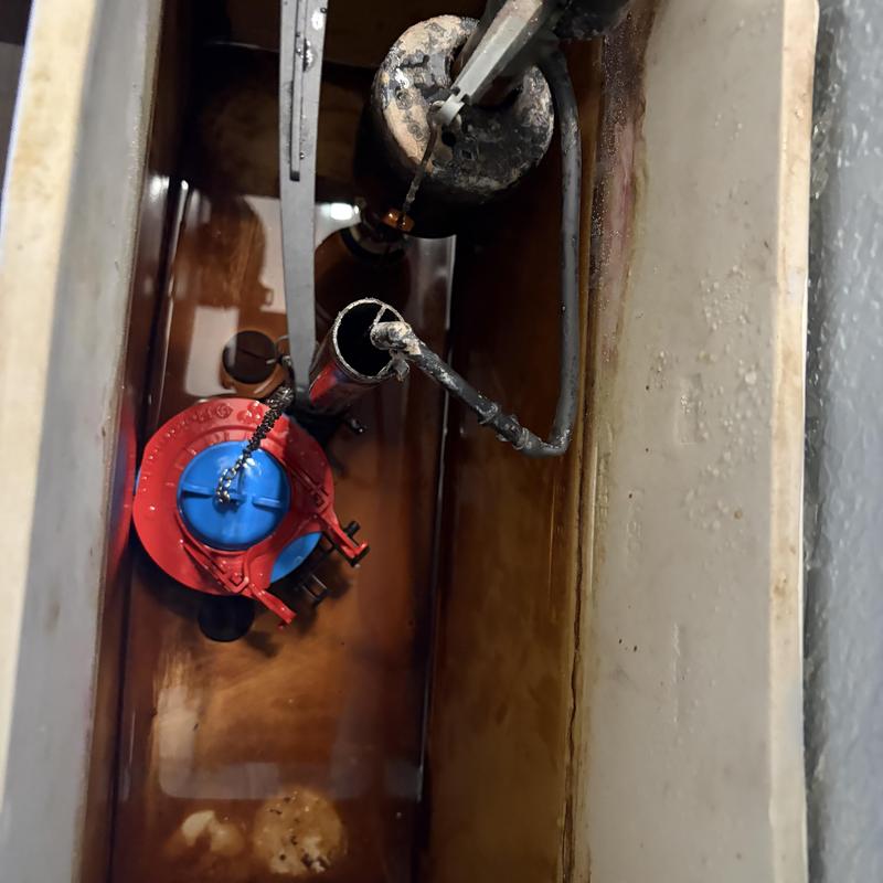 Toilet tank with old flush valve and water stains