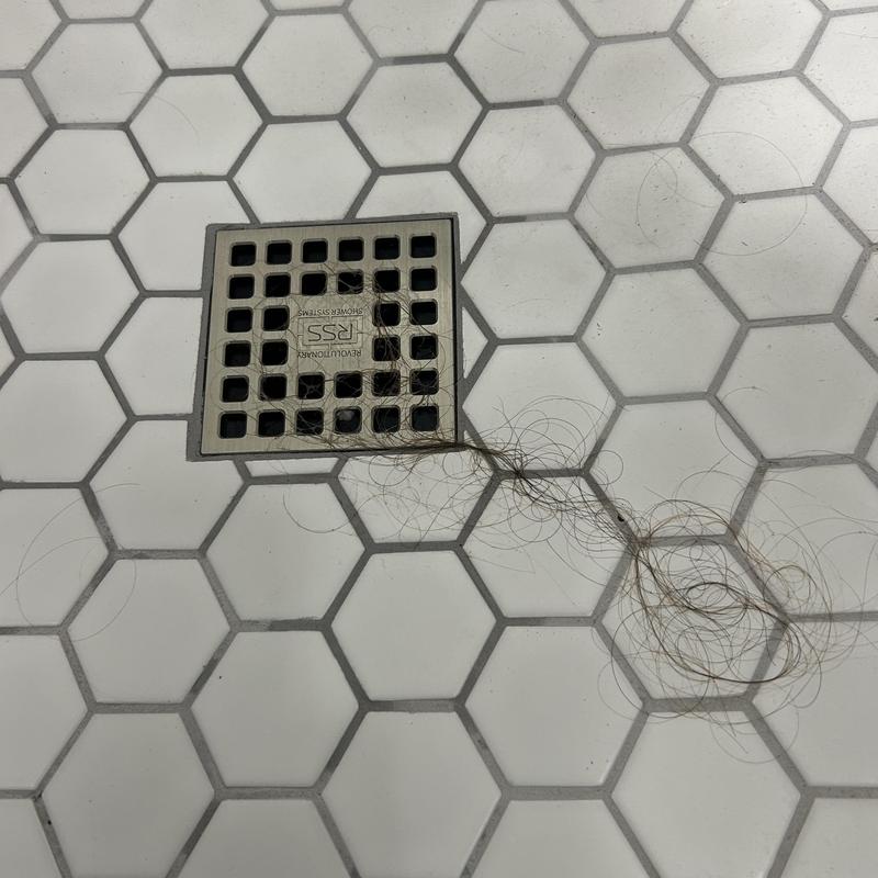 Shower drain with hair clog on tile floor