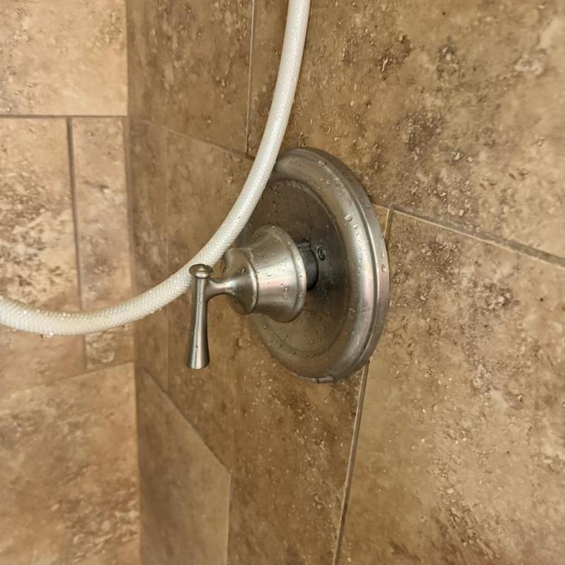 Shower valve handle on tiled wall with hose