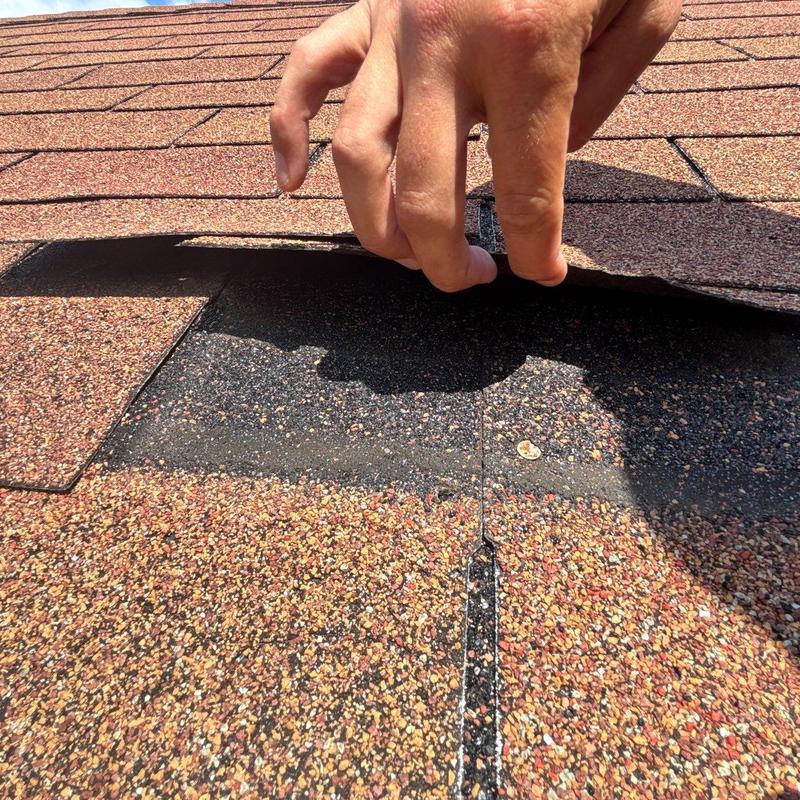 Asphalt roof shingles lifted showing hail damage underneath