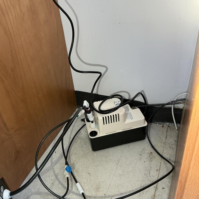 Condensate pump with connected hoses under cabinet