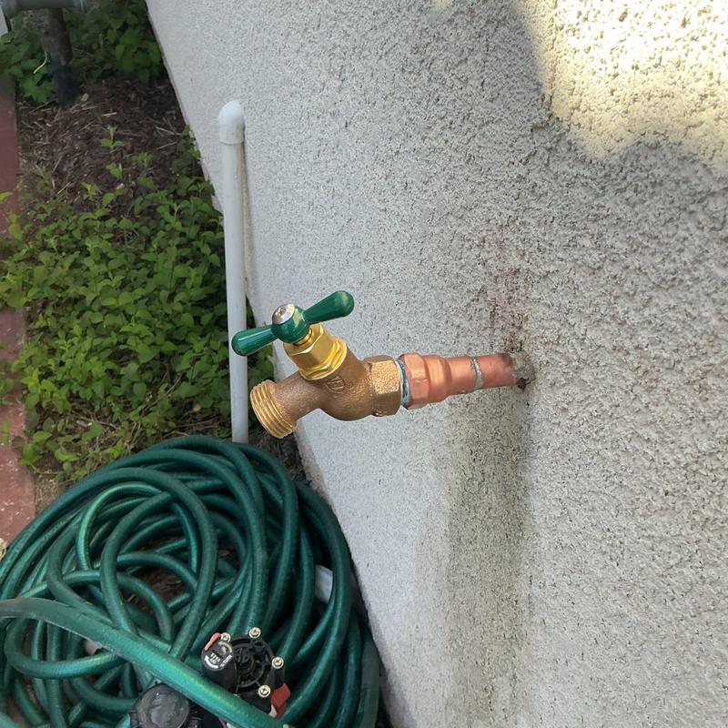 Hose bib with green handle installed on exterior wall