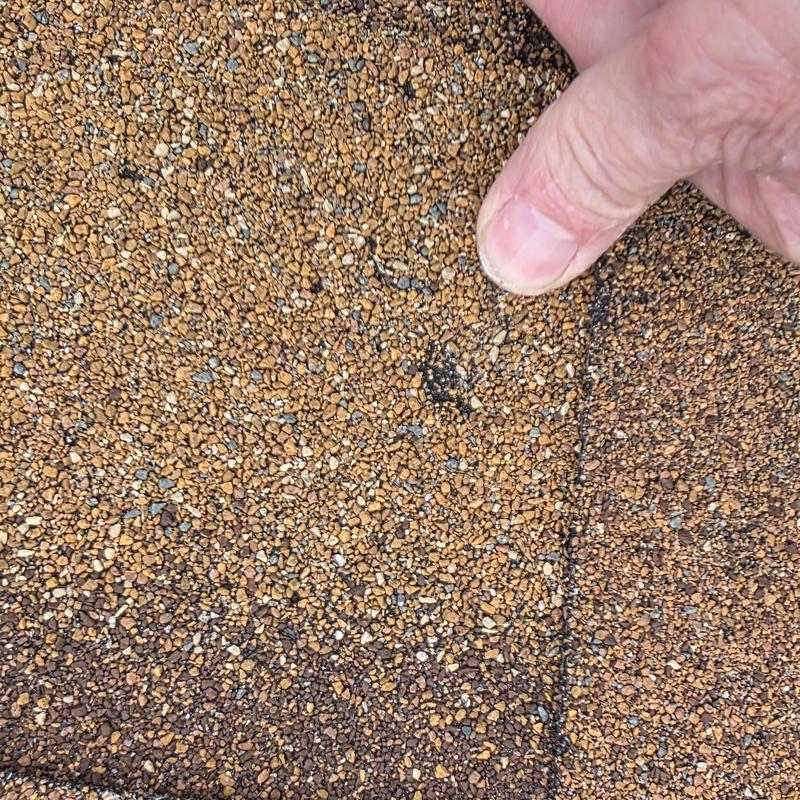 Roof shingle hail damage close-up with finger pointing