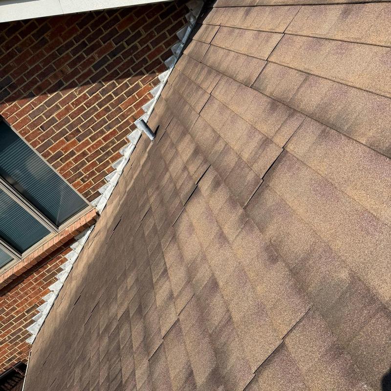 Roof shingles with visible hail damage near brick wall
