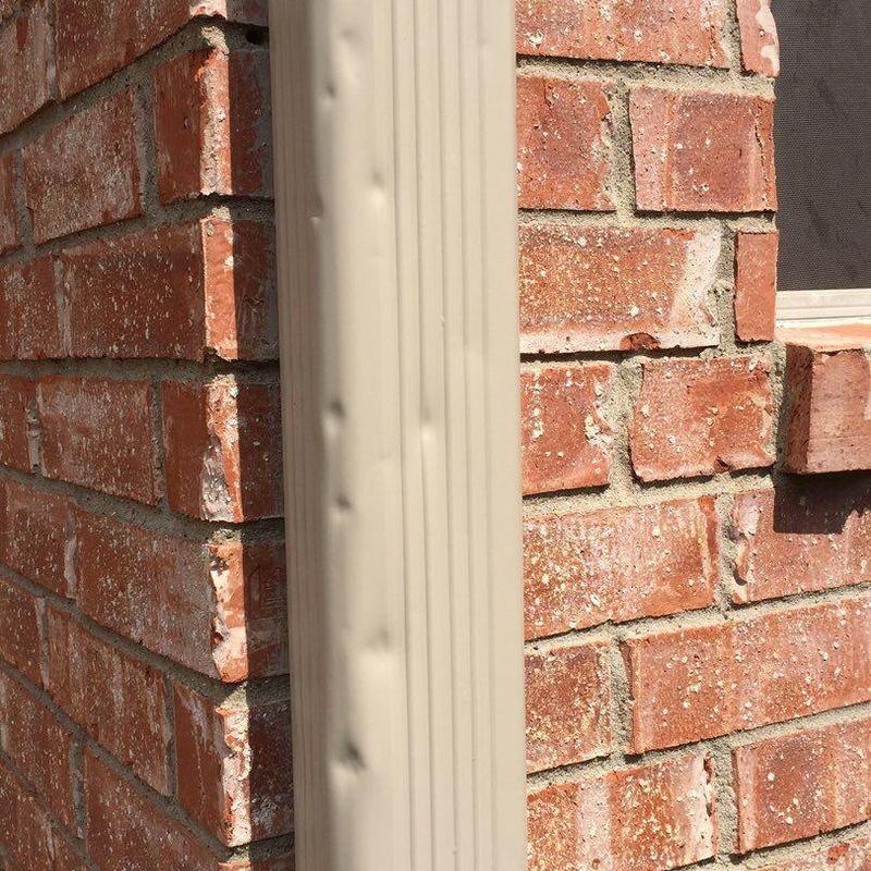 Downspout with hail damage on brick wall exterior