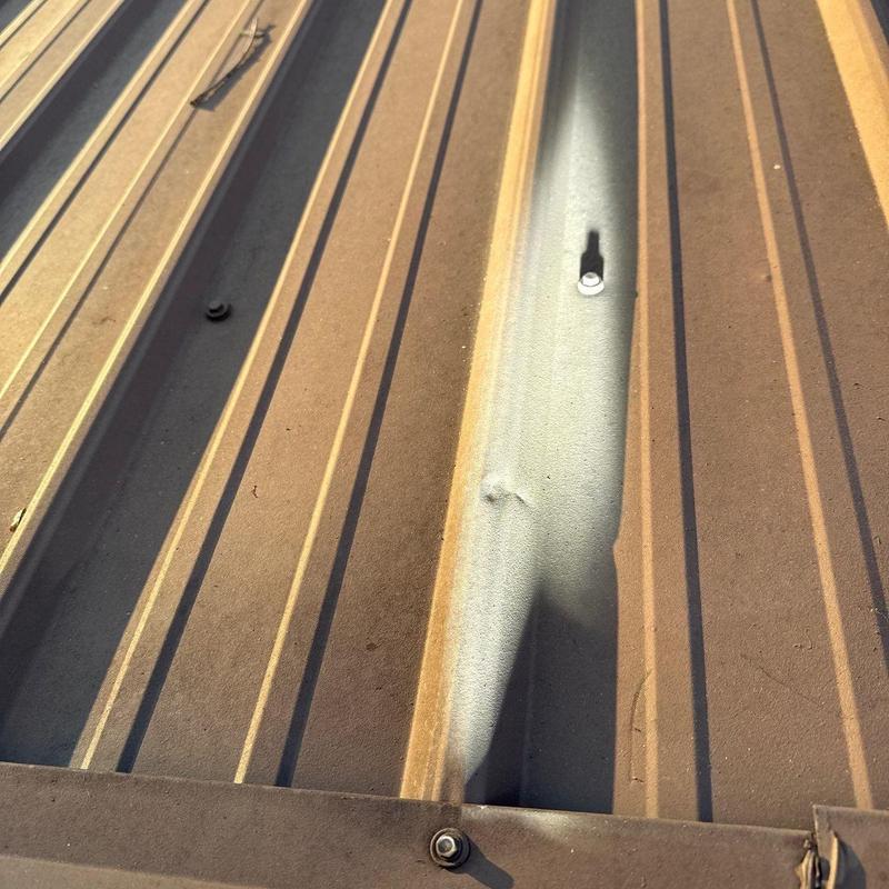 Metal roof panel with hail damage dent and fasteners