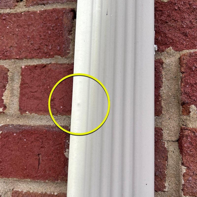 Vinyl siding dent with yellow inspection circle on brick wall