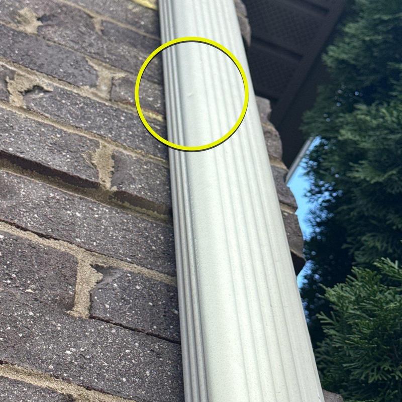 Downspout dent with yellow highlight on brick wall background