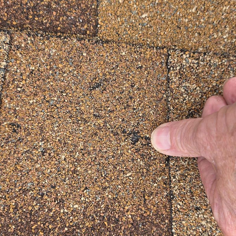 Asphalt shingle hail damage close-up with finger pointing