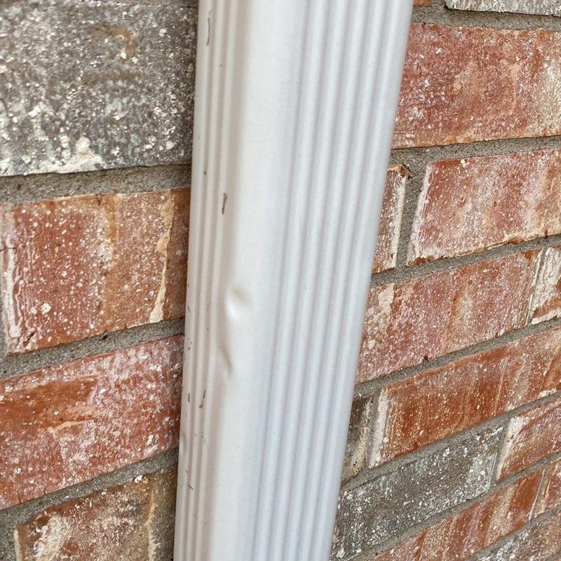Downspout dent damage on brick wall exterior