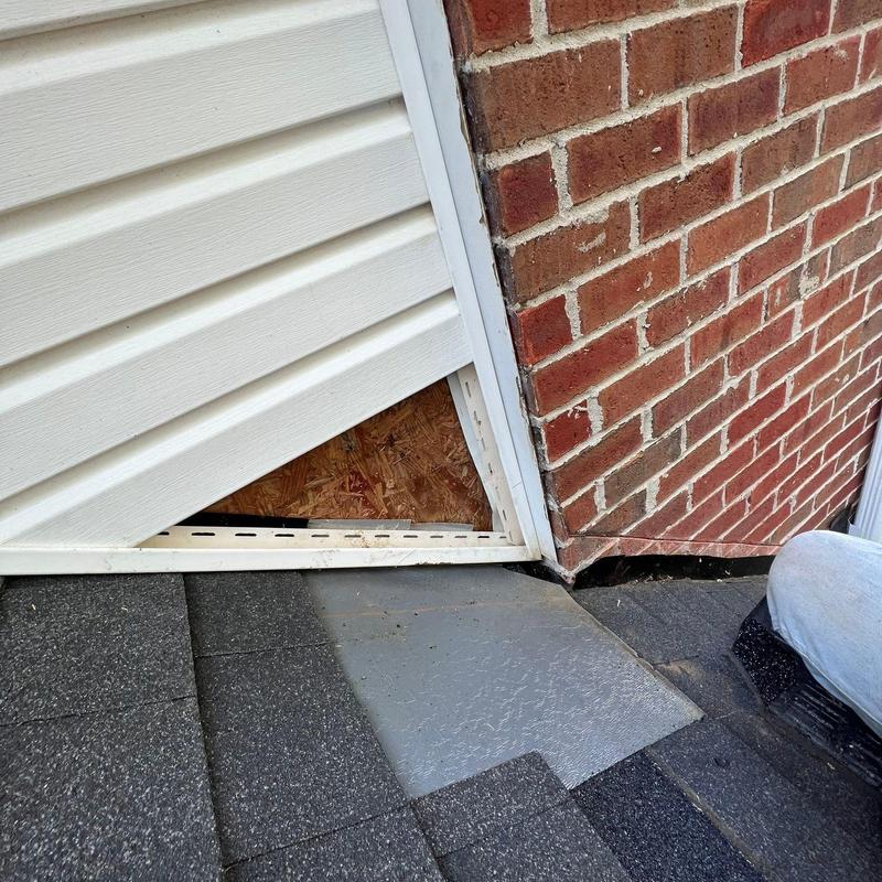 Vinyl siding panel removal near brick chimney on roof