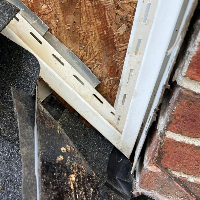 Roof flashing with damaged shingles near brick wall