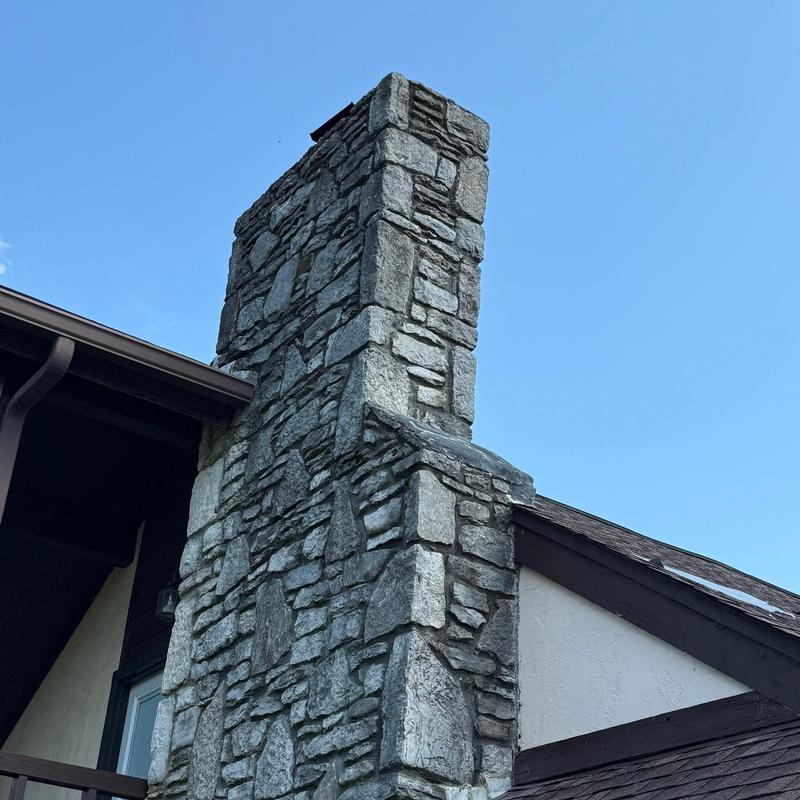 Stone chimney on residential roof with clear sky