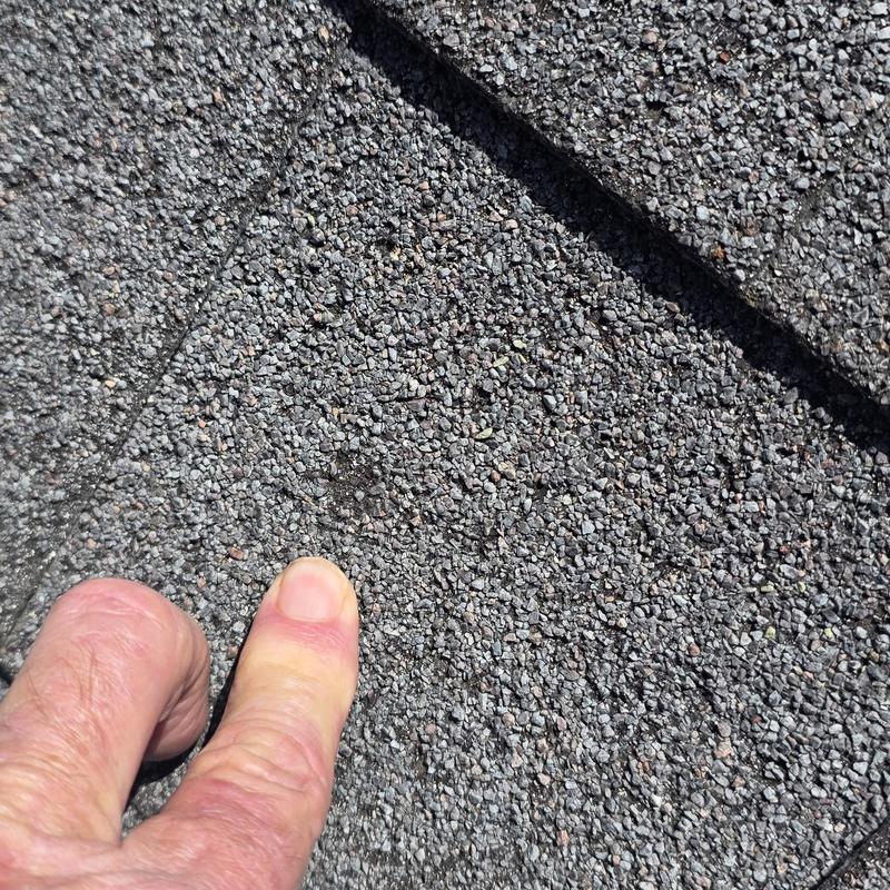 Asphalt shingle roof hail damage close-up with finger