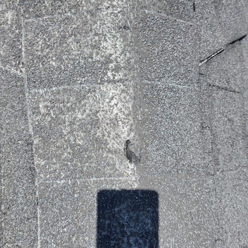 Asphalt roof shingles with hail damage hole