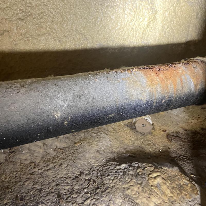 Corroded cast iron drain pipe under exposed wall cavity