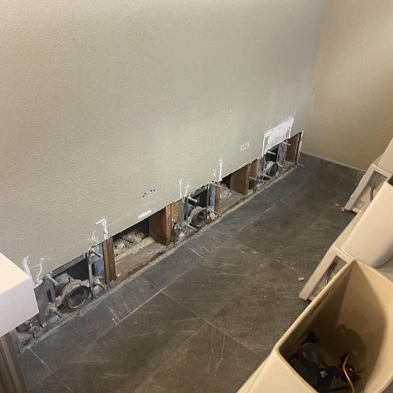 Exposed bathroom drain line behind wall with cracked pipes